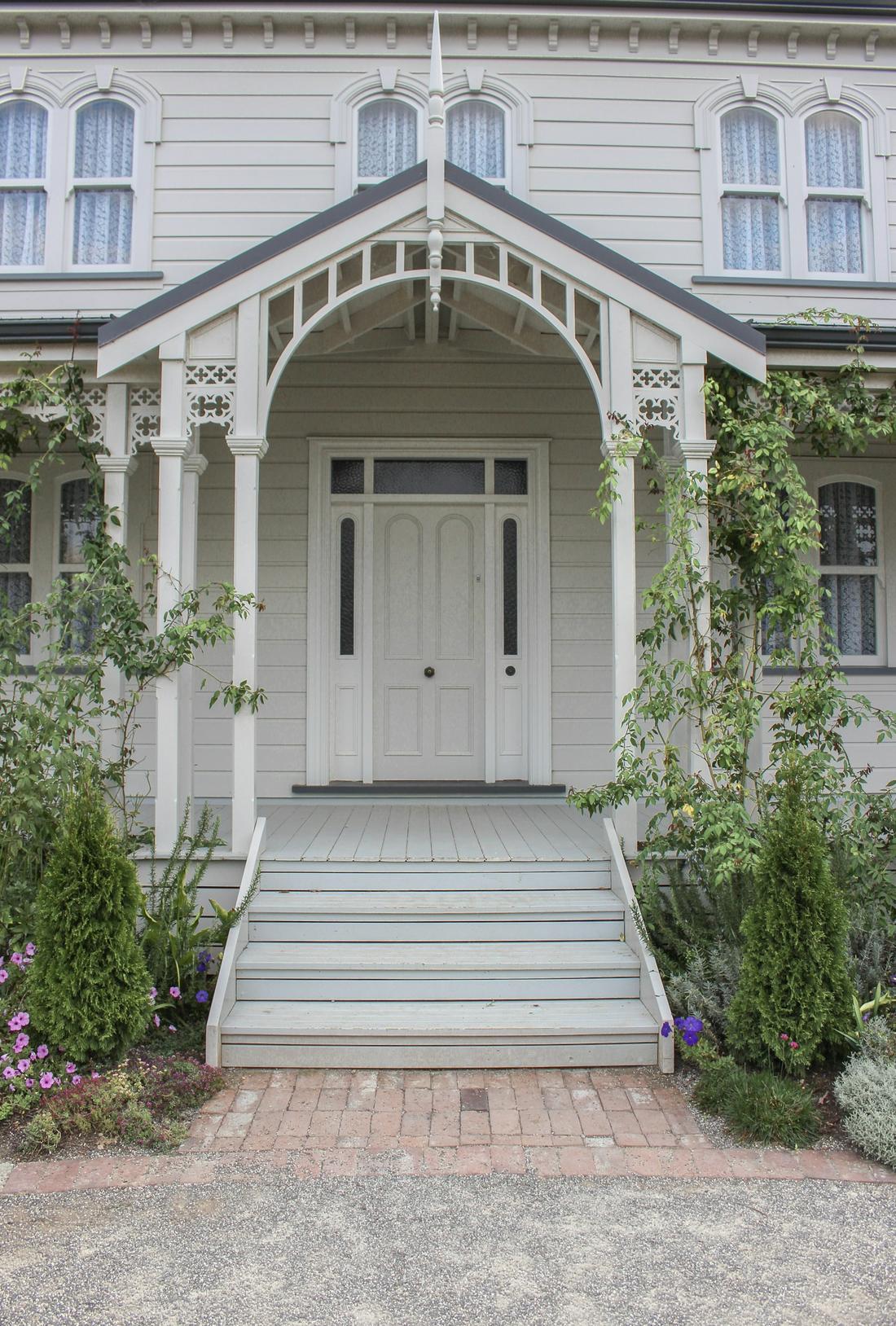White Victorian home with a gabled front porch, steps and climbing roses
