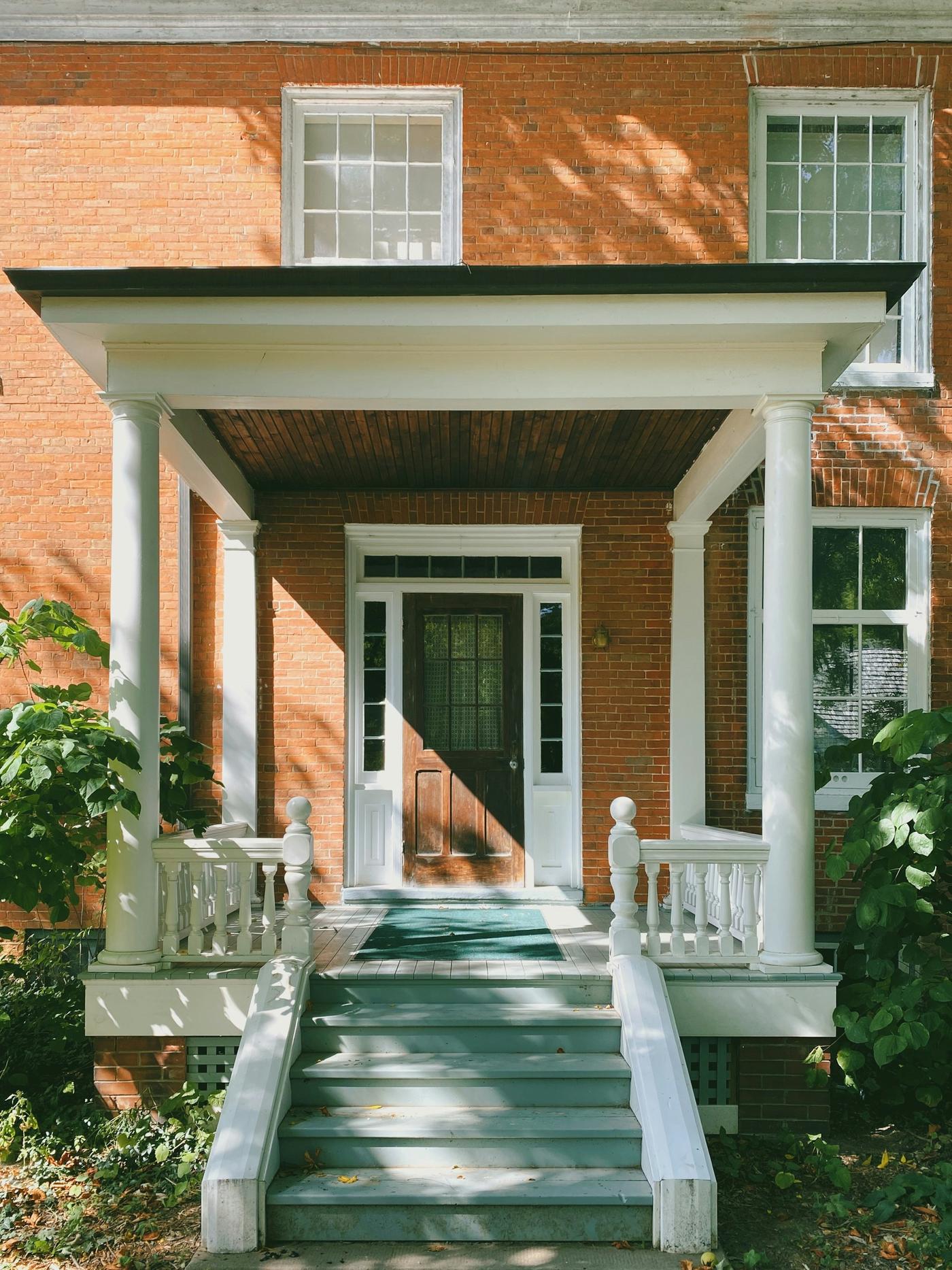 Red brick home with a white columned portico and green front steps in late-day sun